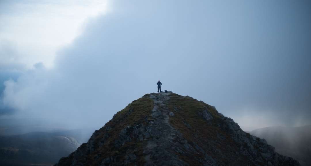 Osoba stojąca na formacji skalnej pod białymi chmurami puzzle online