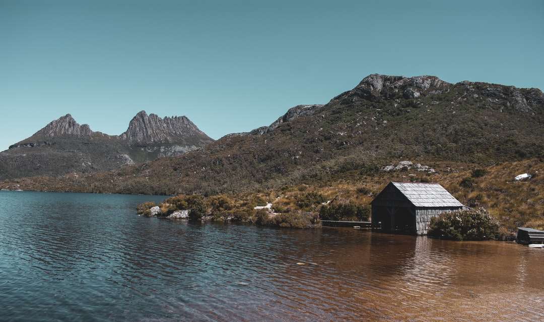 Brązowy drewniany dom w pobliżu jeziora i góry pod błękitne niebo puzzle online