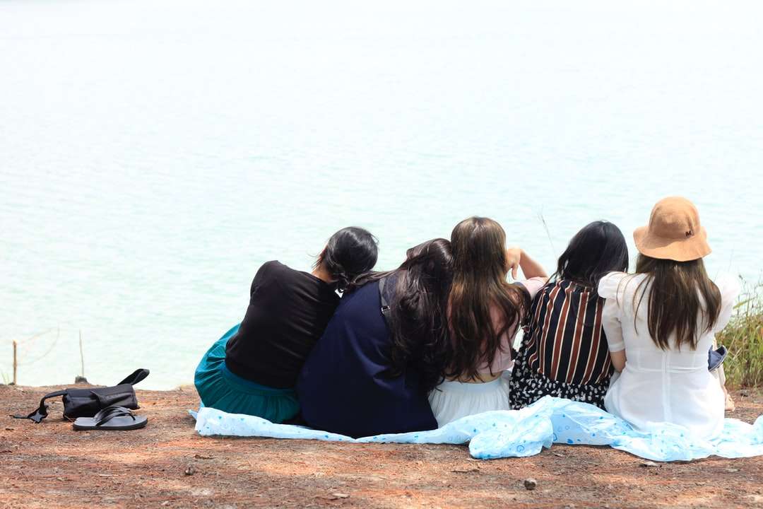 3 kobiety siedzące na brązowym piasku w pobliżu wody puzzle online