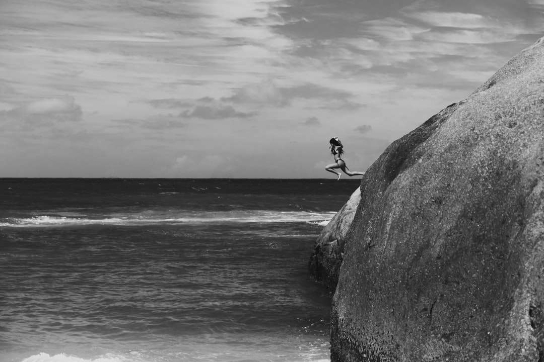 Skala szarości Zdjęcie człowieka siedzi na skale w pobliżu morza puzzle online