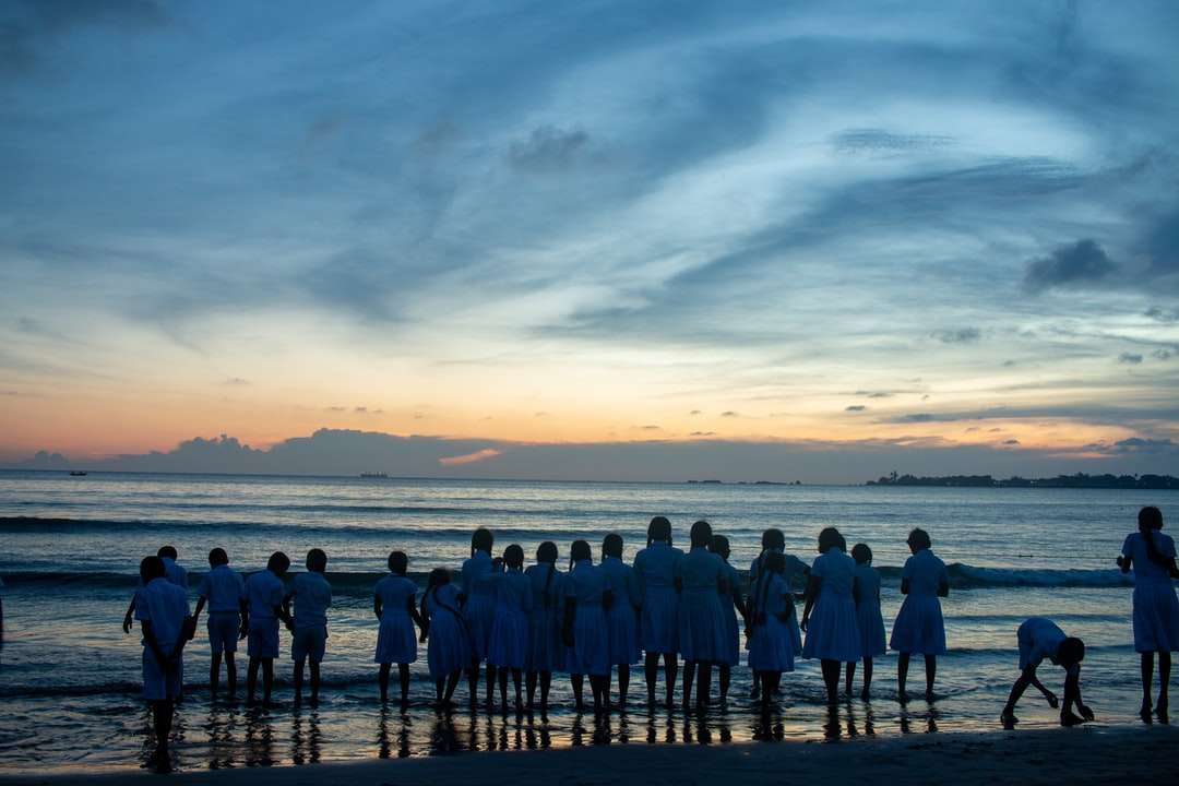 Ludzie stoi na plaży podczas zachodu słońca puzzle online