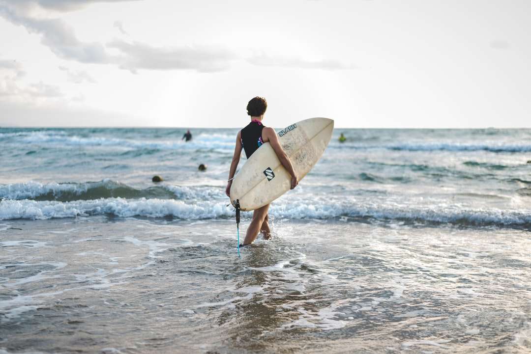 Człowiek w czarnym kombinezonie niosąc białą deskę surfingową puzzle online