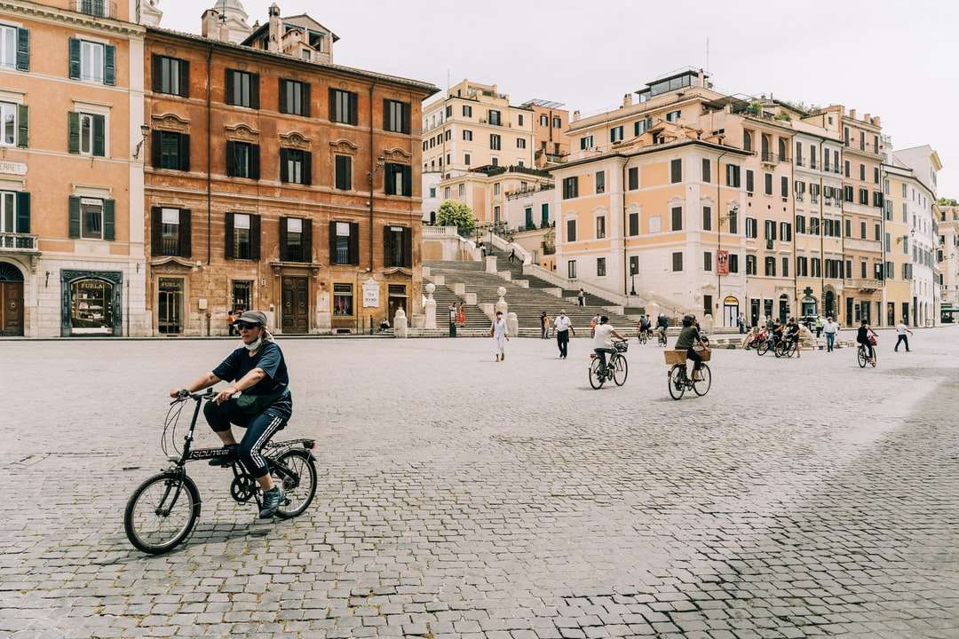 Ludzie jedzie na rowerze na drodze w pobliżu brązowego betonowego budynku puzzle online