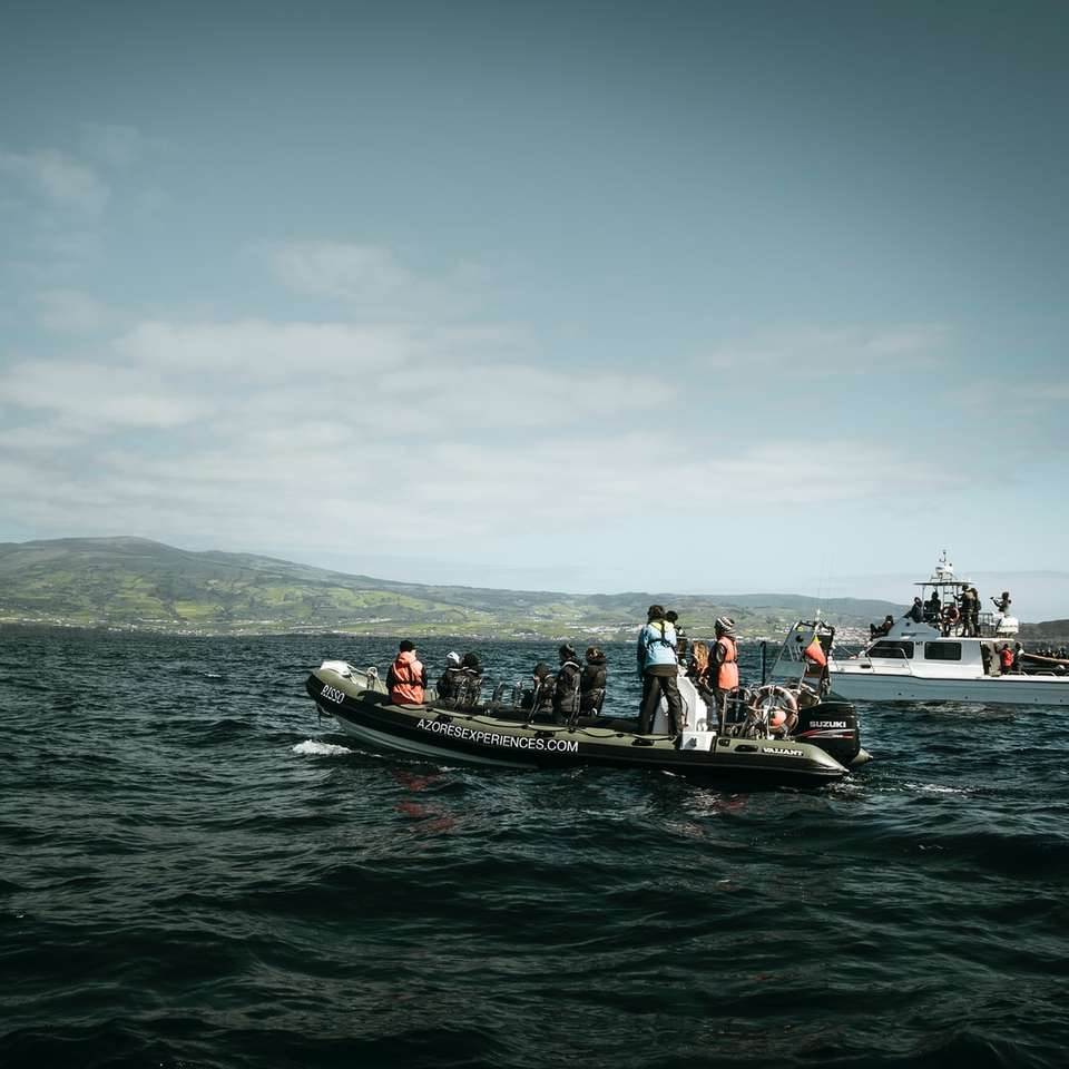 Ludzie jedzie na czarnej i czerwonej łodzi na morzu w ciągu dnia puzzle online