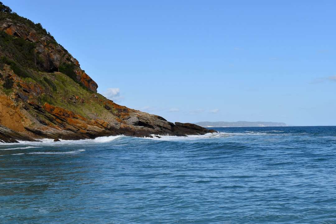 brązowy i zielony formacja skalna obok błękitnego morza puzzle online