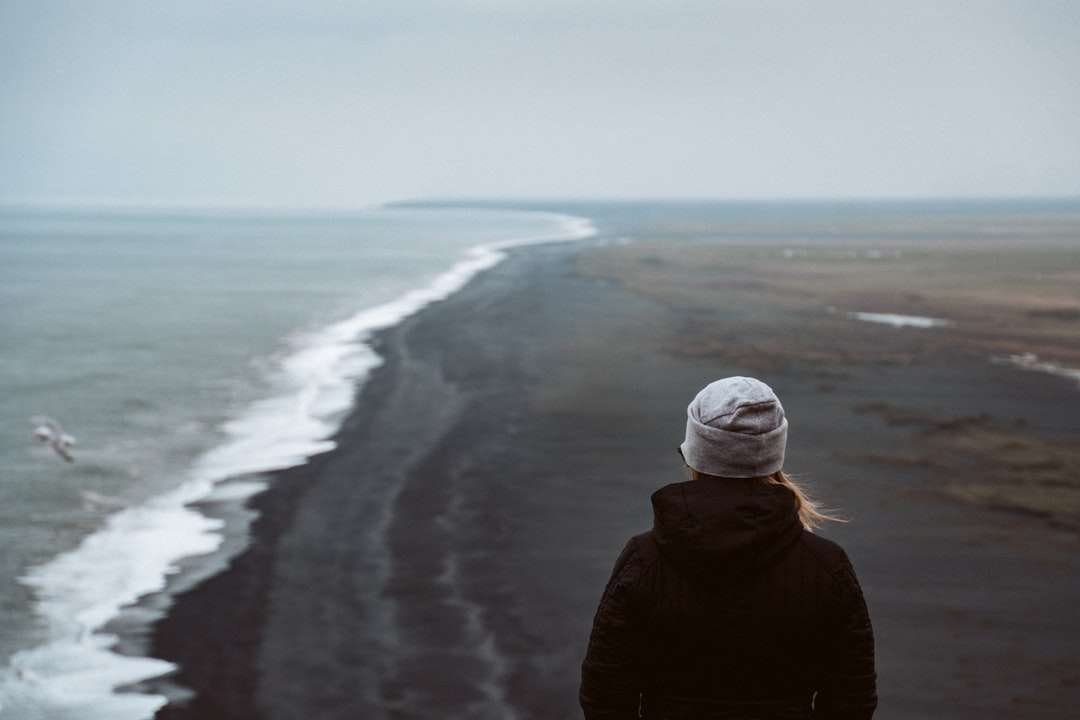 Osoba w czarnej kurtce stojącej na brzegu morza w ciągu dnia puzzle online