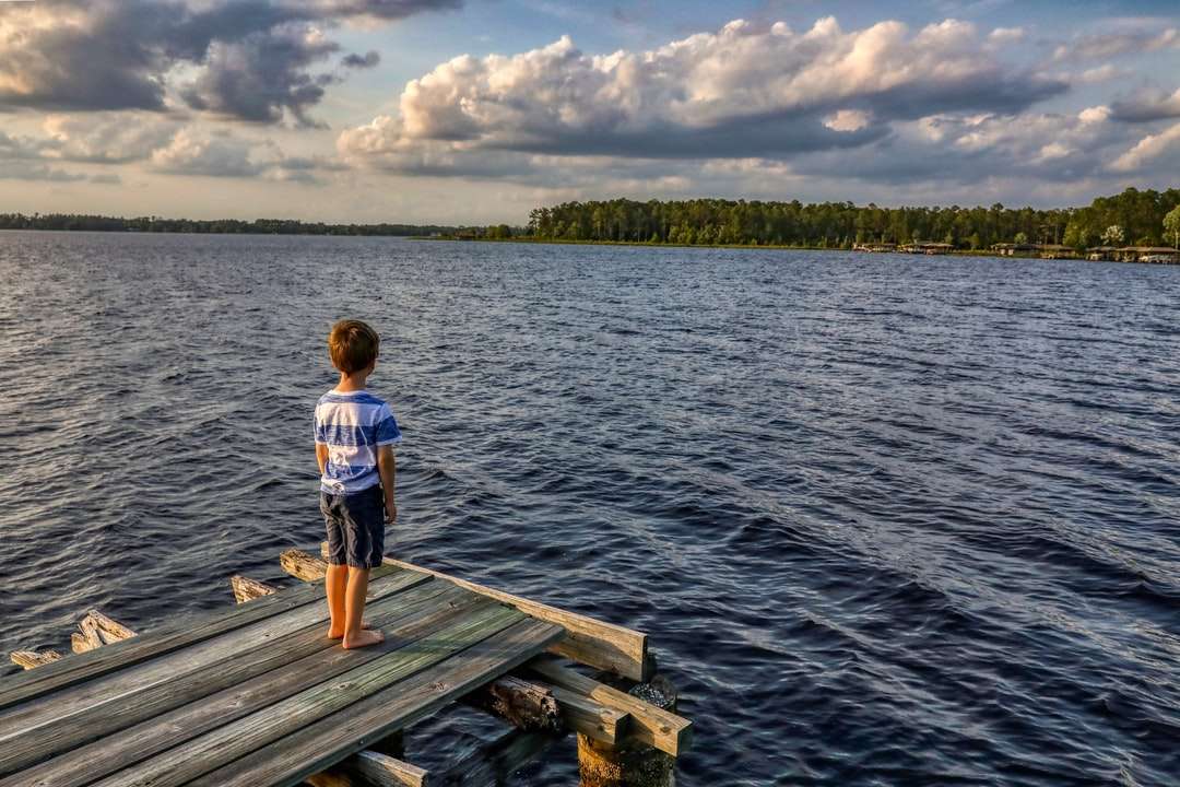 Chłopiec w białej koszulce stoi na drewnianym doku podczas dnia puzzle online