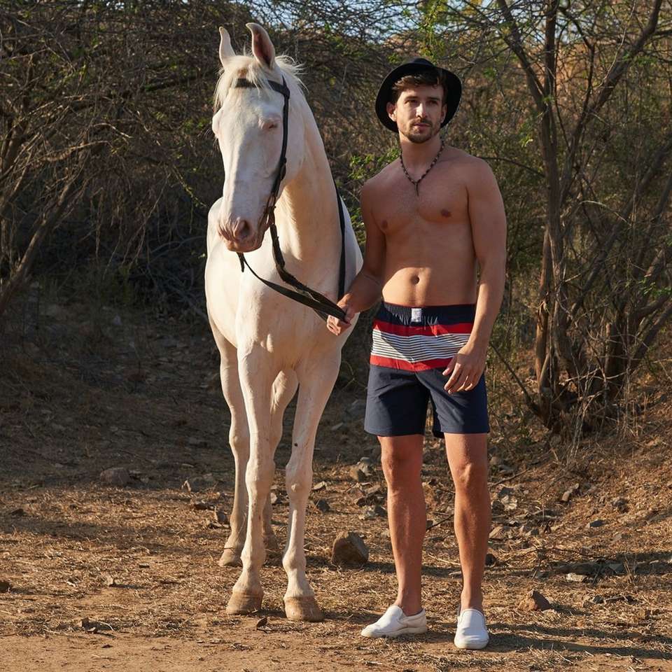 Topless mężczyzna w niebieskich szortach stojących obok białego konia puzzle online