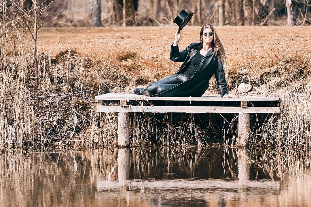 Kobieta w czarnej kurtce siedzi na białej drewnianej ławce puzzle online