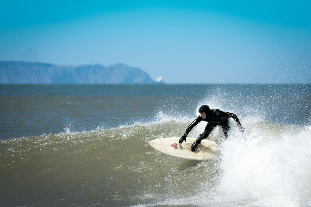 mężczyzna w czarnym kombinezonie surfuje po morzu w ciągu dnia puzzle online