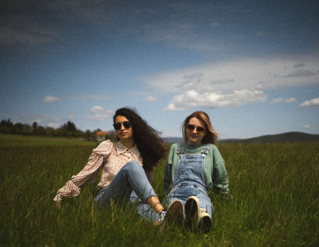 2 kobiety siedzą na polu zielonej trawy pod błękitnym niebem puzzle online