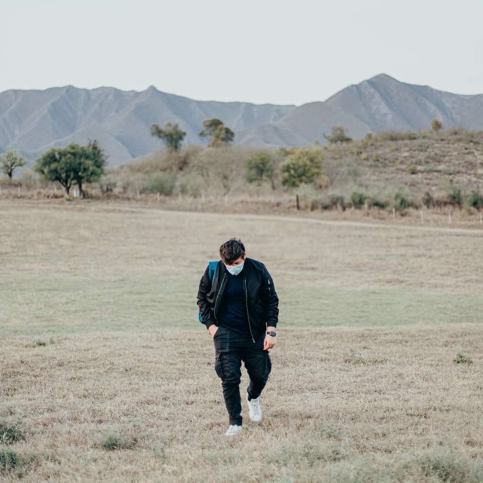 Mężczyzna w czarnej kurtki odprowadzenie na zielonej trawy polu puzzle online