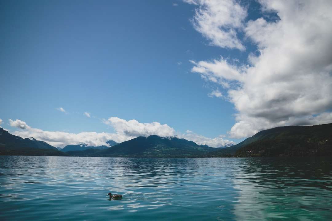 Osoba w łodzi na morzu blisko góry pod błękitnym niebem puzzle online