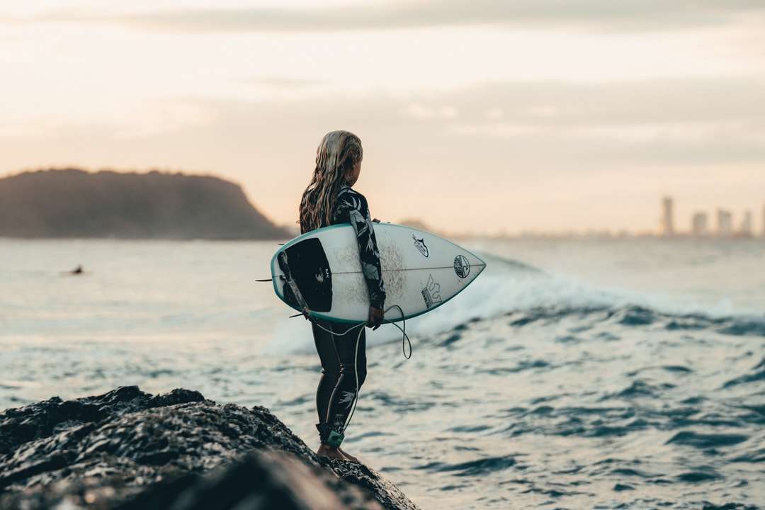 kobieta w czarnym kombinezonie nosząca białą deskę surfingową puzzle online