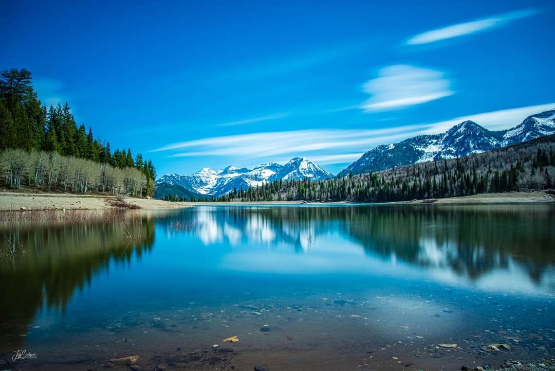 Jezioro otoczone zielonymi drzewami i górami pod błękitnym niebem puzzle online