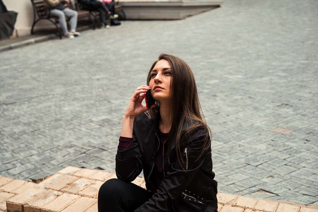 Kobieta w czarnej skórzanej kurtce siedzi na brązowej ceglanej podłodze puzzle online