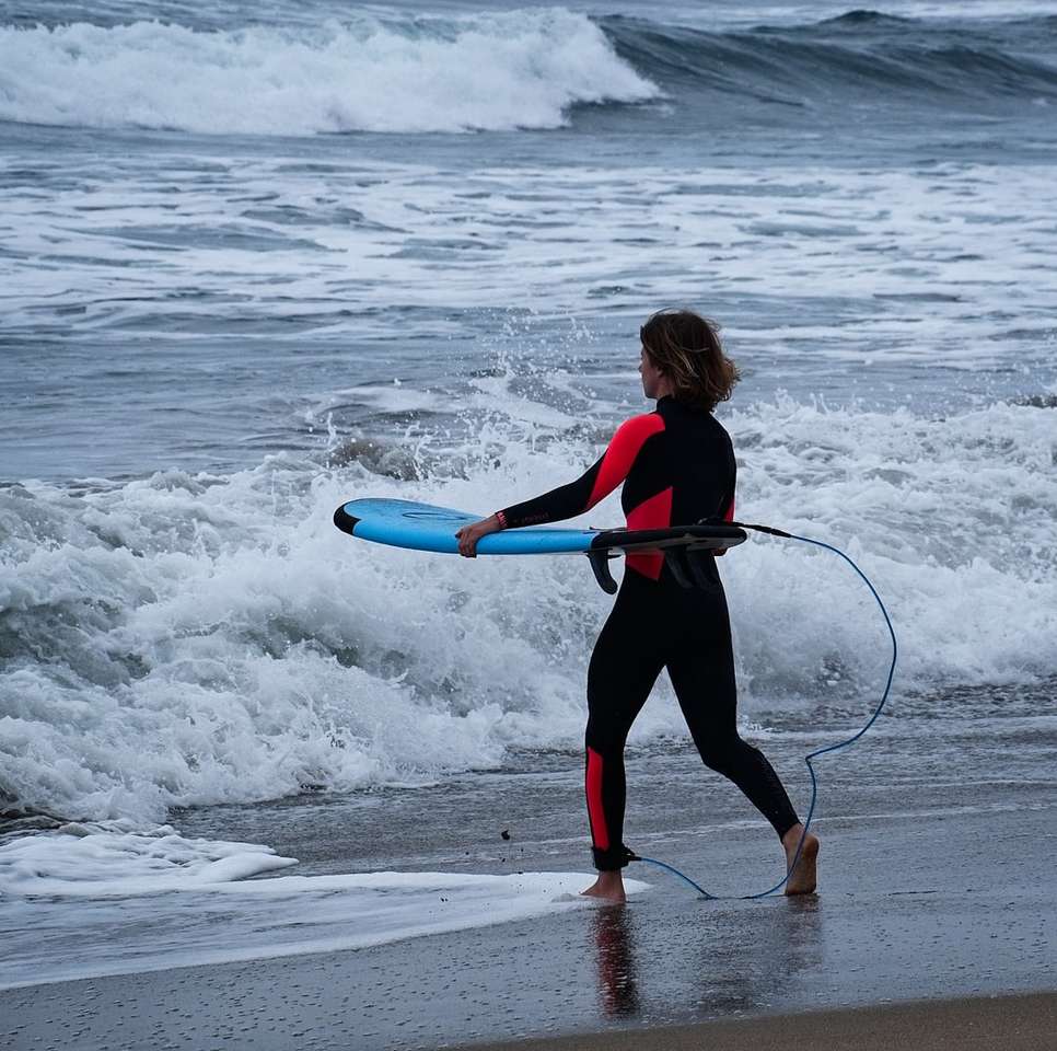 Kobieta w czarnej i czerwonej kurtce gospodarstwa niebieski surfboard puzzle online