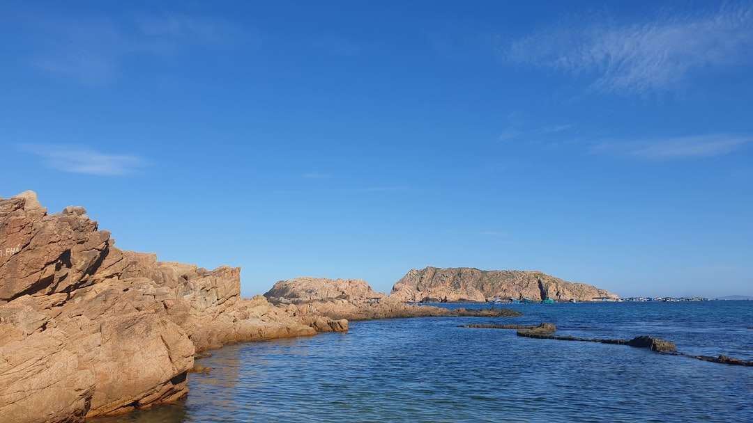 Brązowa formacja skalna obok błękitnego morza pod błękitnym niebem puzzle online