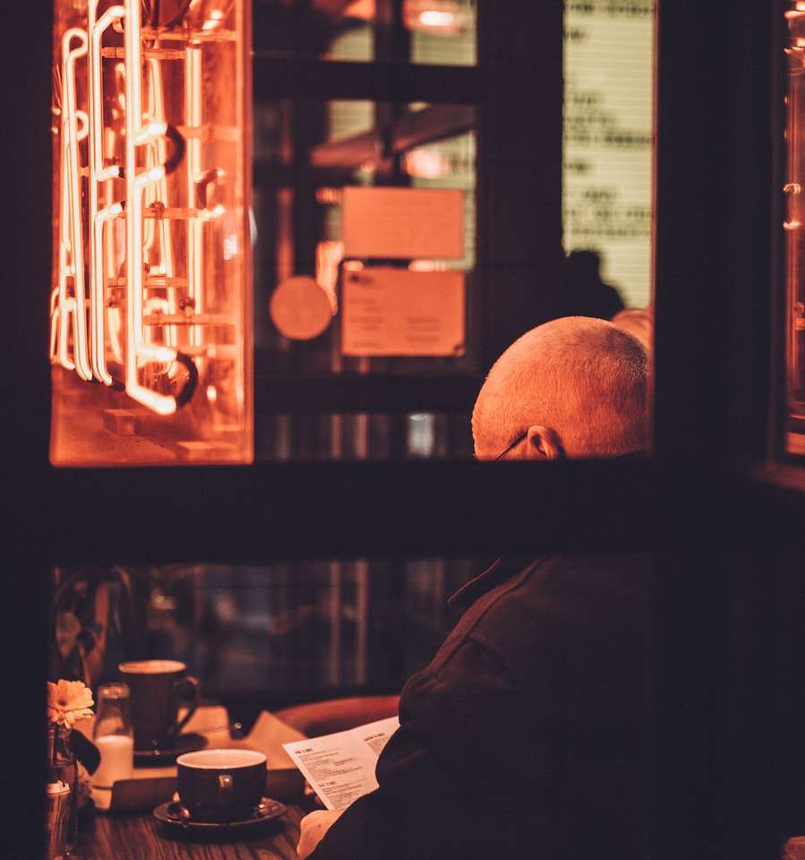mężczyzna siedzący na krześle czytający książkę przed stołem puzzle online