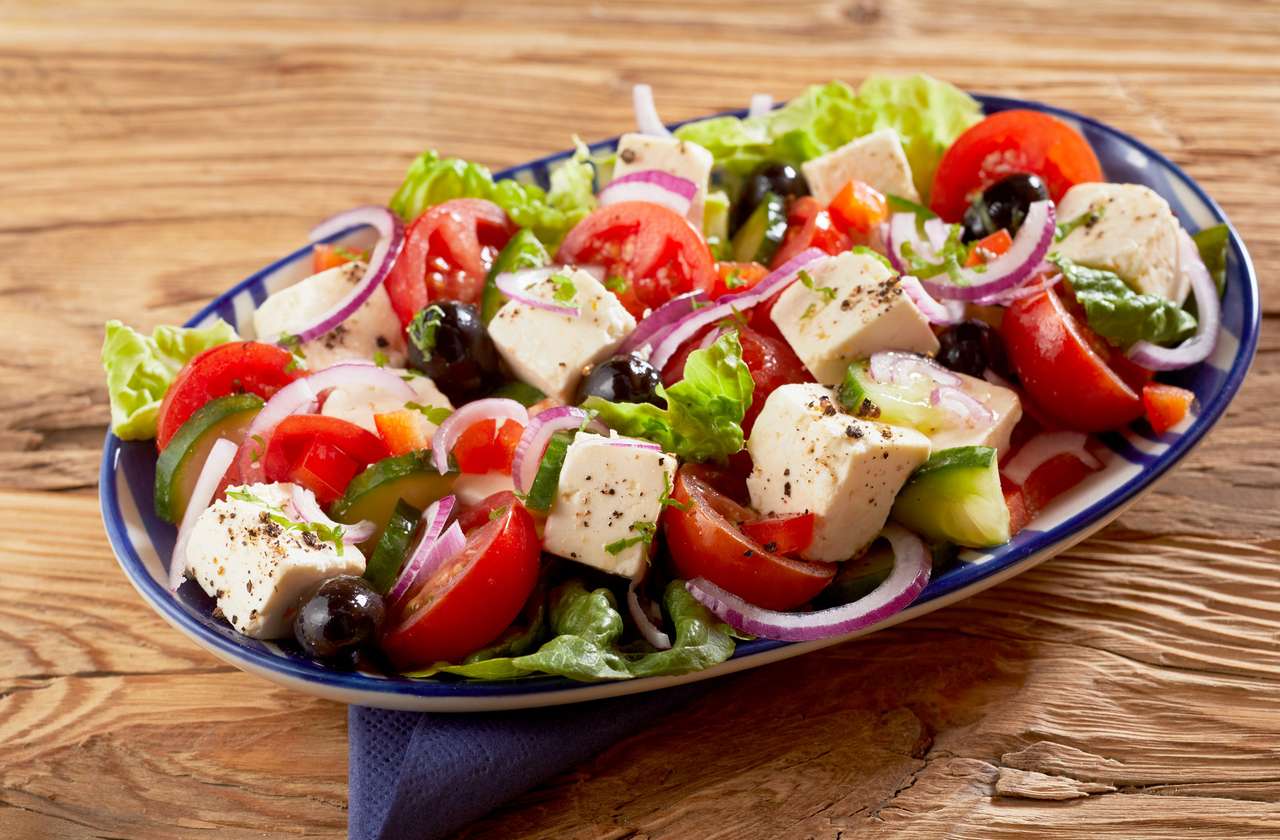 Danie zdrowej świeżej sałatki greckiej z serem feta, oliwkami, ogórkiem, sałatą, cebulą i pomidorem przyprawionym ziołami na drewnianym stole puzzle online
