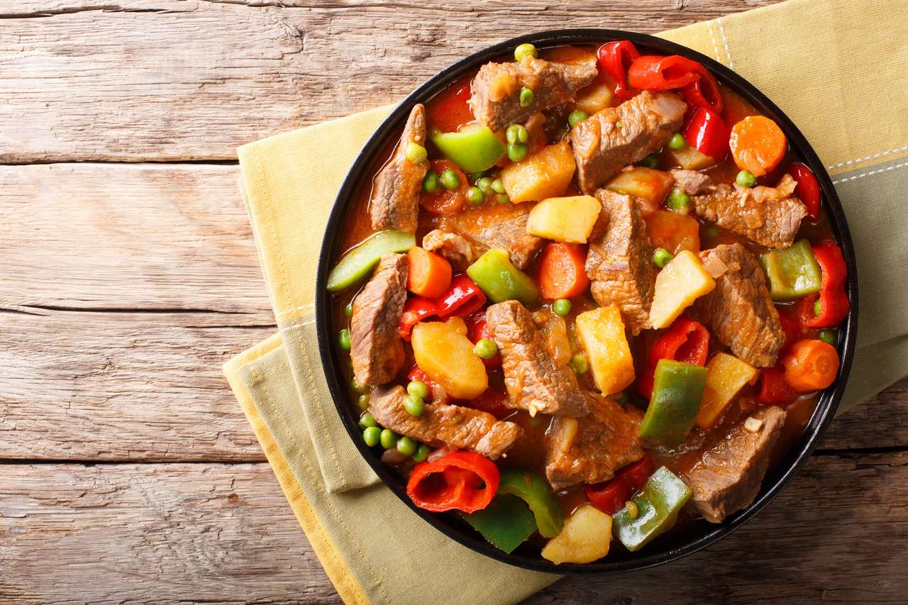 Azjatyckie jedzenie: duszona wołowina z ziemniakami, papryką, groszkiem, pomidorami i marchewkami z bliska na talerzu na stole. puzzle online