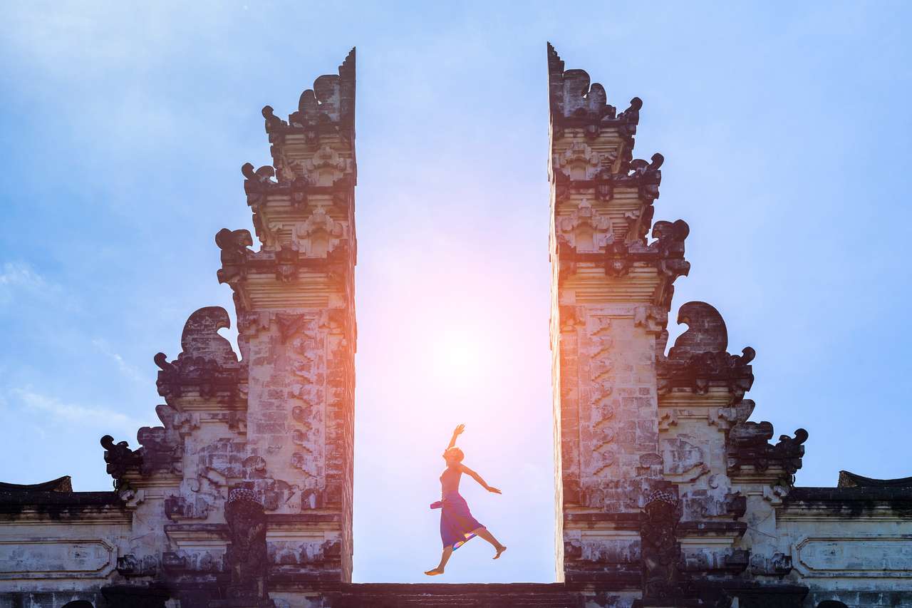 Kobieta podróżnik skoki z energią i witalnością w bramie świątyni, Bali, Indonezja puzzle online