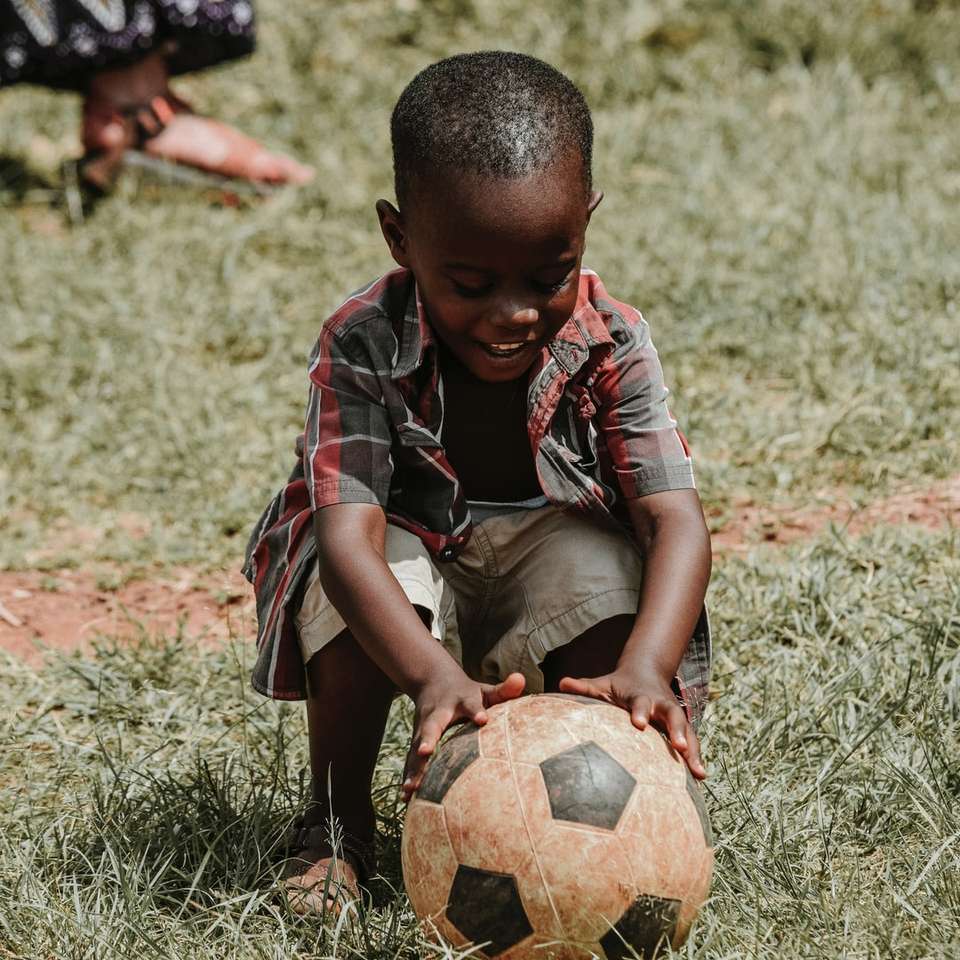 uśmiechnięty chłopiec siedzi trzymając piłkę nożną w ciągu dnia puzzle online