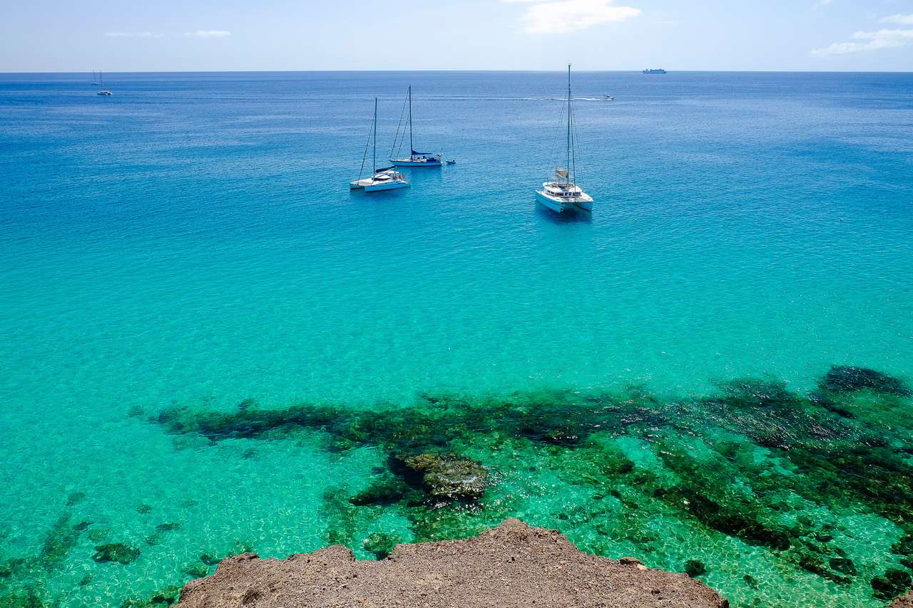 Widok na ocean z krystaliczną wodą i trzema łodzią woutistic w Morro Jable na wyspie kanaryjskiej Fuerteventura, Hiszpania. puzzle online