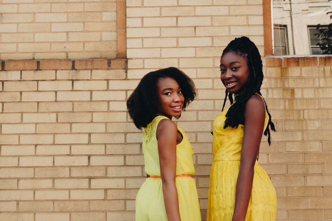 Dwie kobiety na sobie żółte sukienki bez rękawów w pobliżu brązowej cegły puzzle online