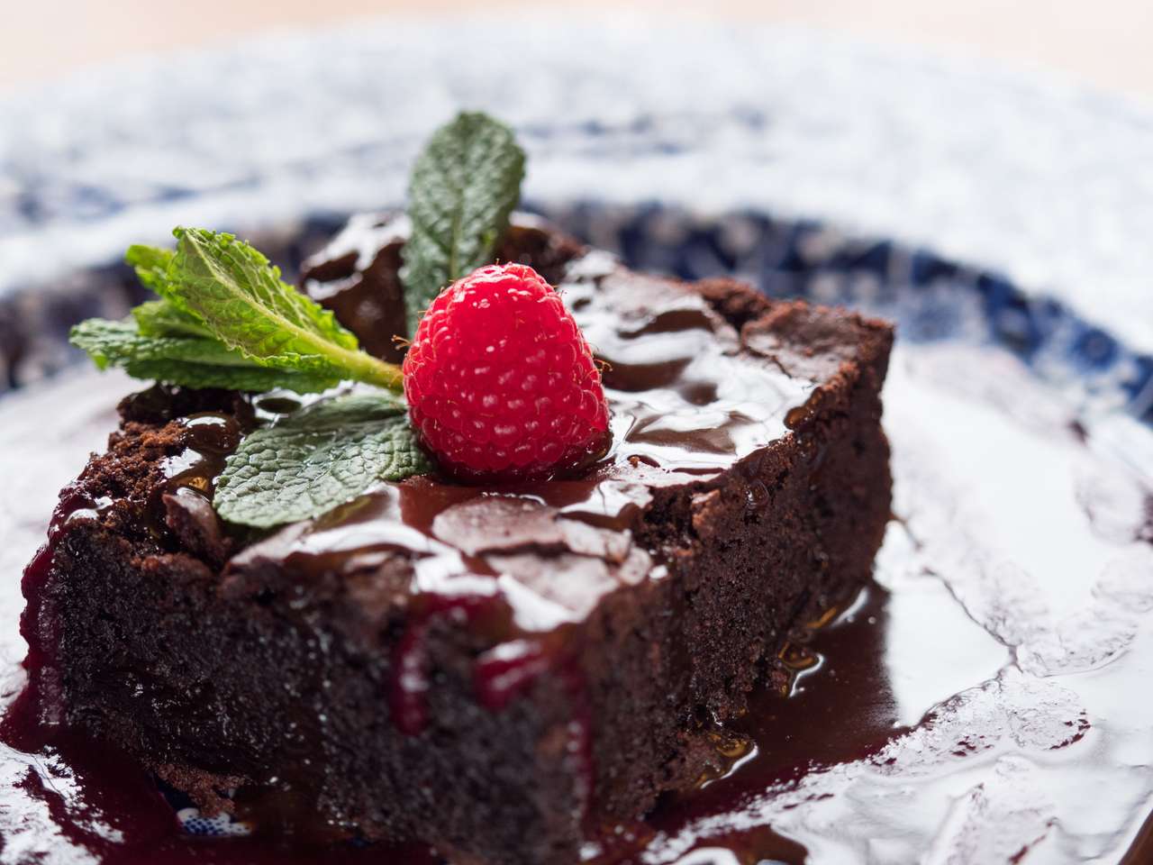 Bliska plasterek ciasto czekoladowe serwowane na talerzu z sosem czekoladowym. Malinowe owoce i liście mięty na górze. Naturalne okno światła. puzzle online