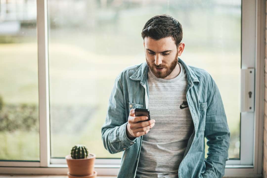 mężczyzna trzymający smartfon przy oknie puzzle online