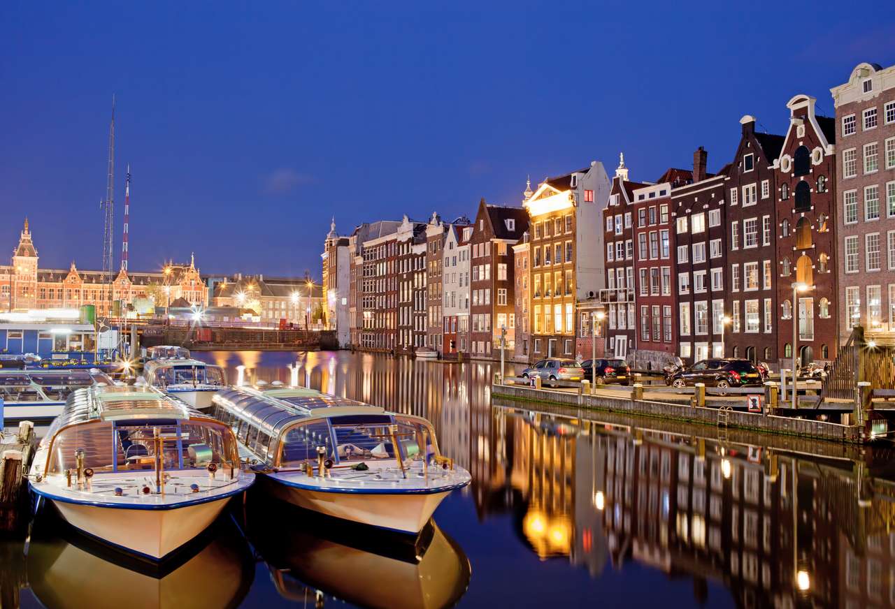 Miasto Amsterdam w Holandii w nocy, historyczne domy mieszkalne z odbiciami na wodzie i łodzie gotowe do kanałów wycieczek i rejsów. puzzle online