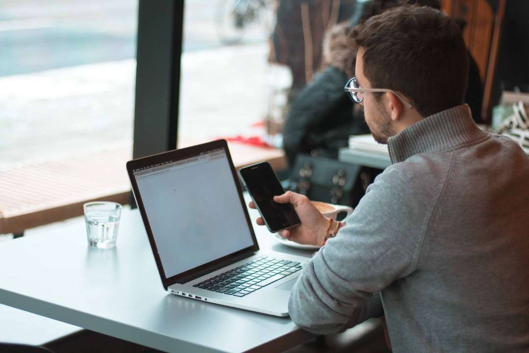 mężczyzna siedzący przy stole z laptopem i smartfonem puzzle online