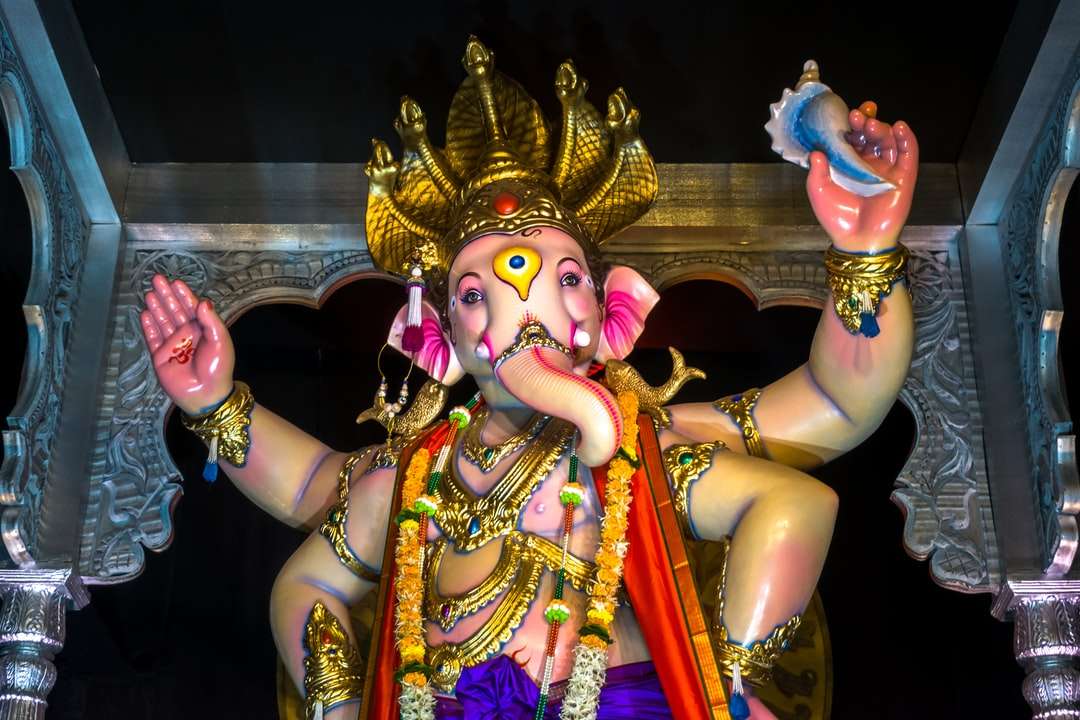 posąg hinduskiego bóstwa przed złotą i fioletową ścianą puzzle online