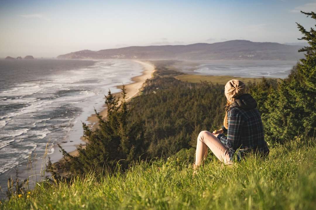 osoba siedząca na wzgórzu w pobliżu oceanu w ciągu dnia puzzle online