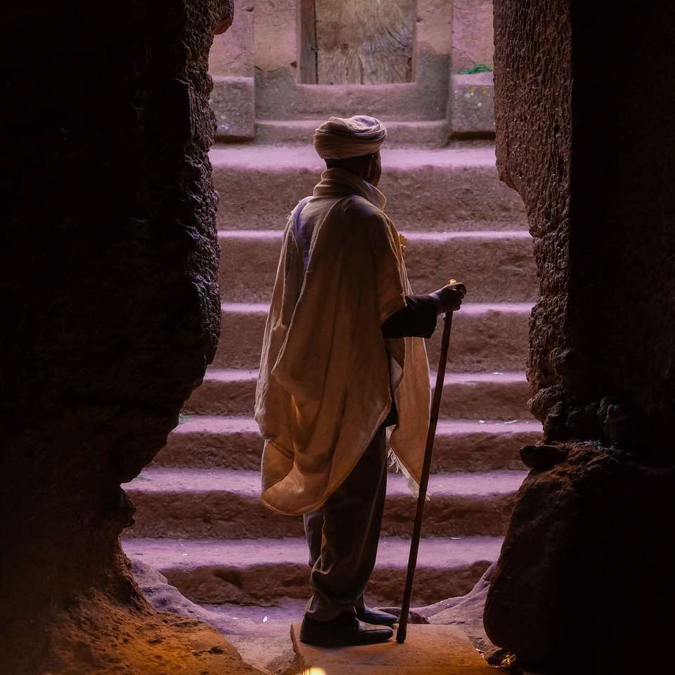 mężczyzna stojący na wejściu do jaskini z brązowego kamienia, trzymający laskę puzzle online