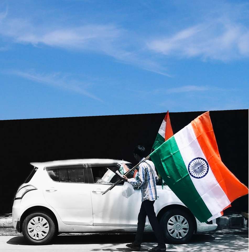 mężczyzna trzymający flagę Indii obok białego samochodu puzzle online