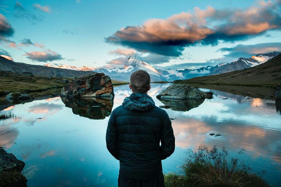 mężczyzna stojący przed widokiem na jezioro otoczone górami puzzle online
