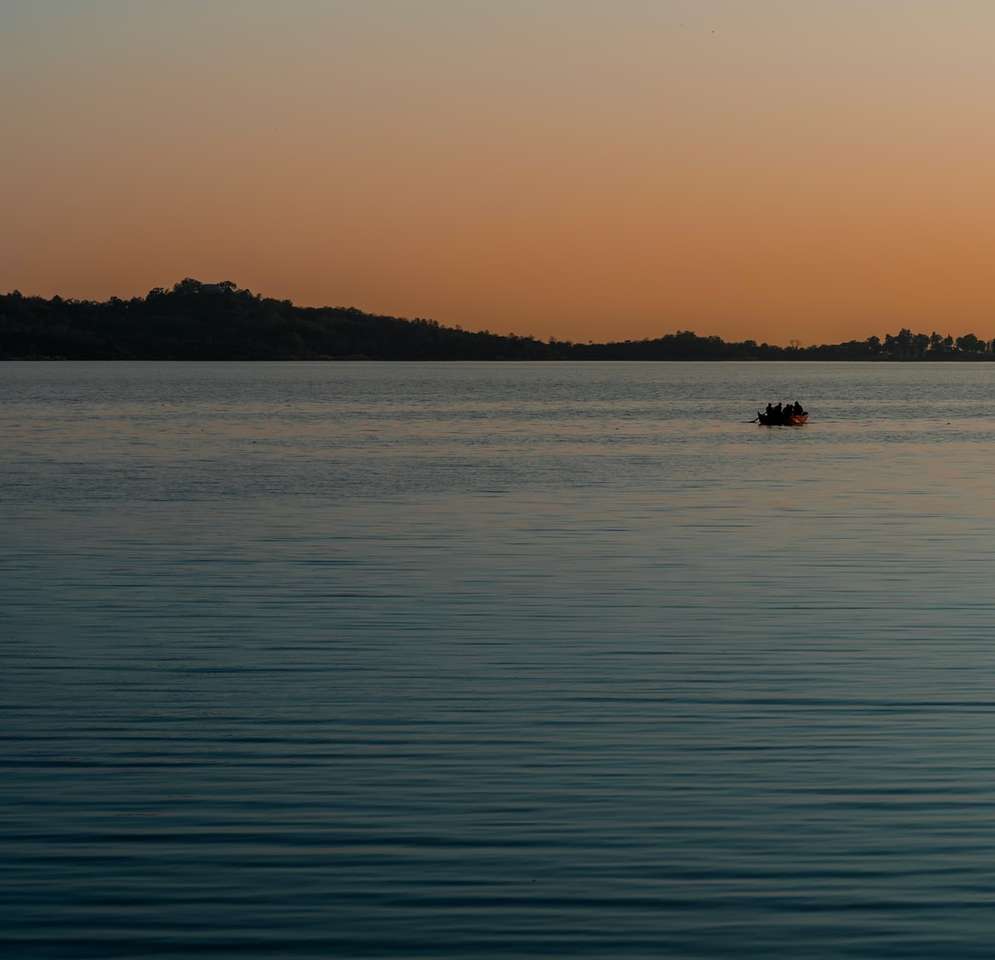 sylwetka osoby płynącej łodzią po morzu podczas zachodu słońca puzzle online