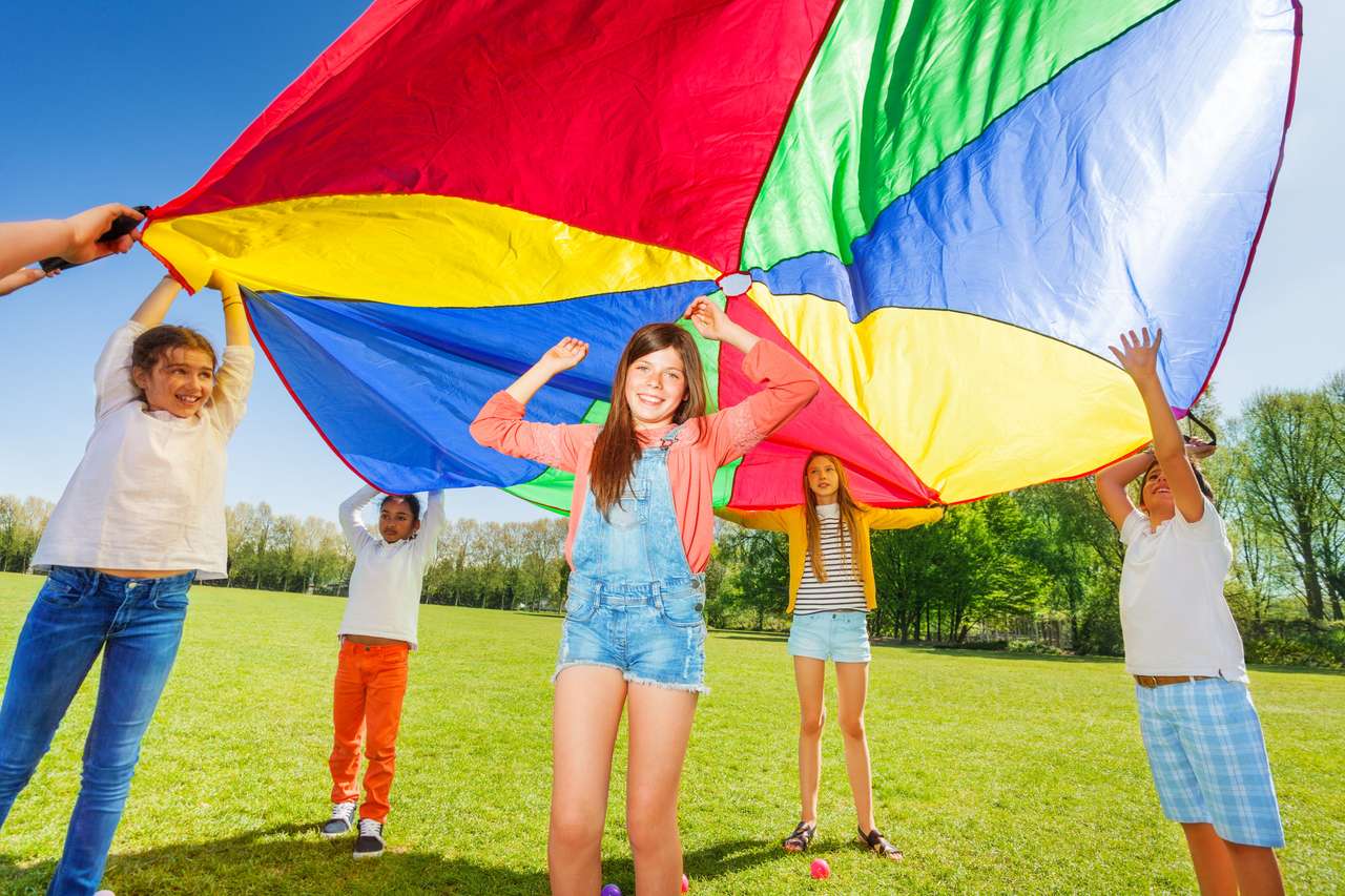 Dzieci bawiące się tęczowym spadochronem w parku puzzle online