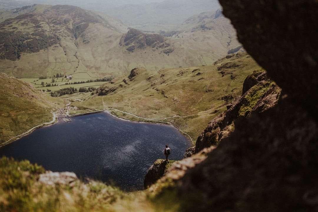 osoba w czarnej kurtce stojąca na formacji skalnej w pobliżu jeziora puzzle online