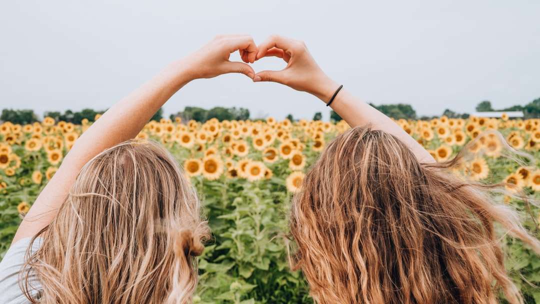 dwie kobiety formujące serce za pomocą rąk stojących przed polem słonecznika puzzle online